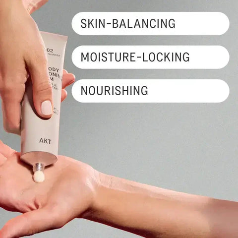 A hand squeezing a beige tube of body cream into another hand, with three white text labels reading 'SKIN-BALANCING', 'MOISTURE-LOCKING', and 'NOURISHING' on a soft gray background.
