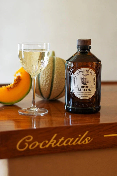 Bottle of Brut Melon liqueur with a glass of melon liqueur and a cantaloupe on a wooden surface.