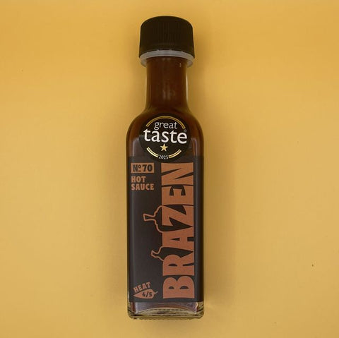 A bottle of Great Taste Brazen No.70 Hot Sauce on a solid yellow background.