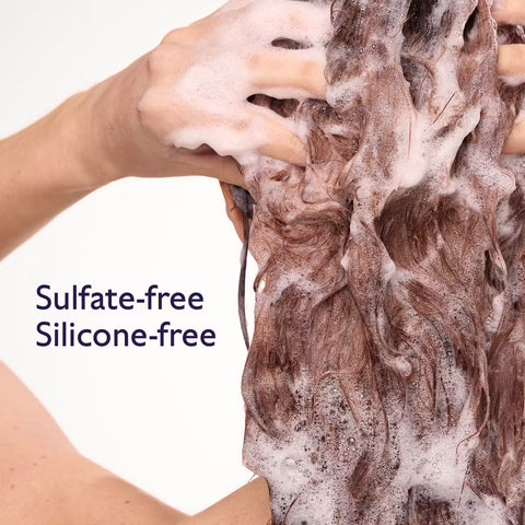 Close-up of a person washing long brown hair with thick white foam, with text reading 'Sulfate-free Silicone-free' on a white background.
