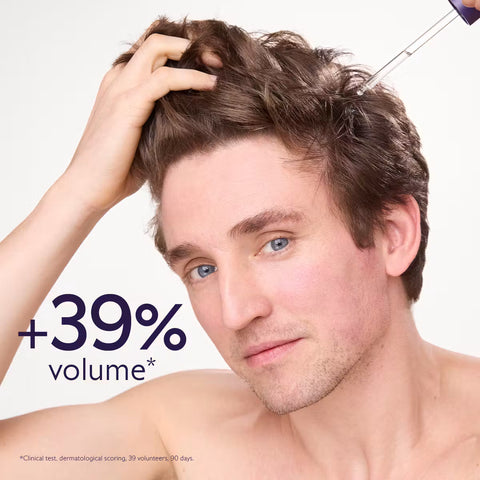 A close-up of a man with voluminous brown hair, holding his hair with one hand, with a hair-thinning treatment tool visible near his scalp. Text on the image reads '+39% volume*'.