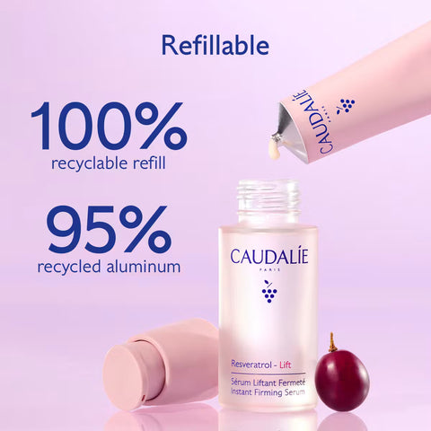 Caudalé Paris refillable serum bottle shown with a pink applicator tube being dispensed, a second tube lying on its side, and a small red fruit on a soft lavender background. Large text highlights recyclable refill and recycled aluminum.