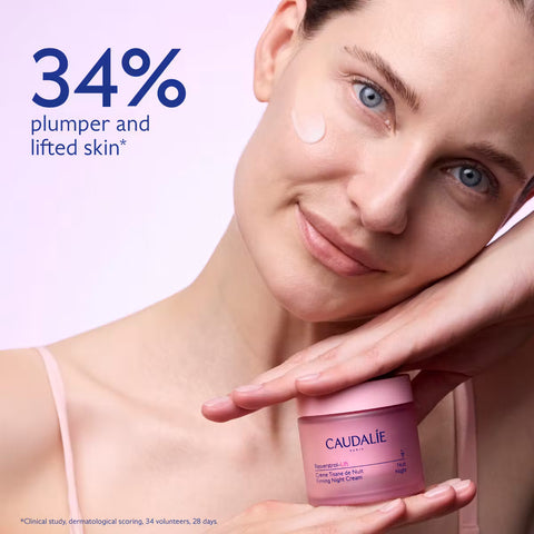 A woman holds a pink Caudalie Regenerating B5 Night Cream jar while applying cream to her cheek. The image features a light pink background with promotional text reading '34% plumper and lifted skin'.