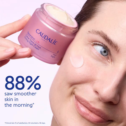 A close-up beauty ad showing a woman applying or wearing a pink jar of Caudalíe overnight cream, with a dollop of cream on her cheek and large Spanish text reading '88% notaron la piel más suave por la mañana'.