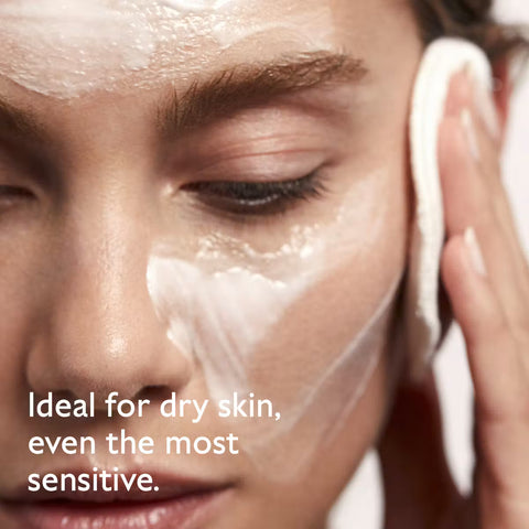 Close-up of a person applying or cleansing cream onto their face with a cotton pad, with text overlay reading 'Ideal for dry skin, even the most sensitive.'.