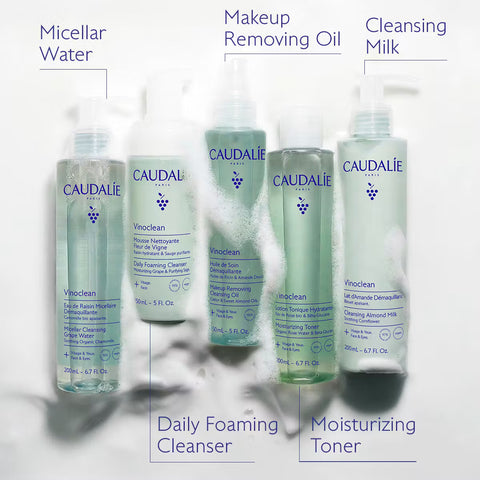 Four Caudalie skincare bottles arranged on a white background with text labels pointing to each product: Micellar Water, Makeup Removing Oil, Cleansing Milk, Daily Foaming Cleanser, and Moisturizing Toner.