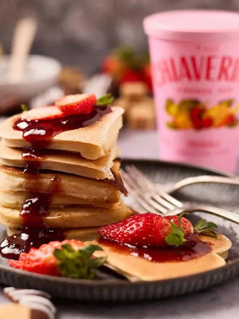 Stack of pancakes with syrup and strawberries on a plate, with a container of Haagen-Dazs ice cream in the background.