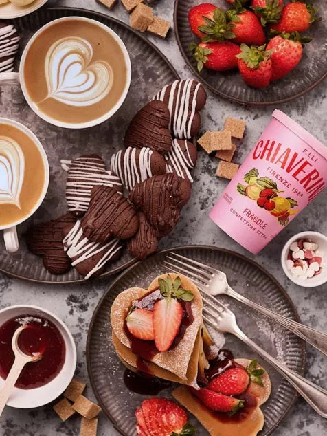 Café setting with pastries, coffee, and strawberries on a rustic surface.