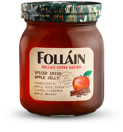 A glass jar of Folláin Spiced Irish Apple Jelly with a decorative green and white patterned lid, set against a plain white background.