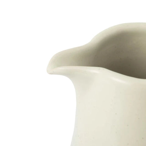 Close-up of a ceramic pitcher with a rounded, hand-drawn spout and a speckled off-white glaze, shown against a plain white background.