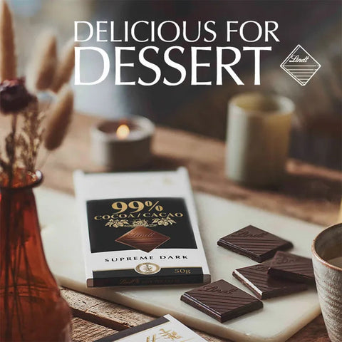 A bar of Lindt Supreme Dark chocolate is displayed on a marble board with several chocolate pieces, set in a cozy, warm environment with candles and dried flowers. Large white text at the top reads 'DELICIOUS FOR DESSERT' alongside the Lindt logo.