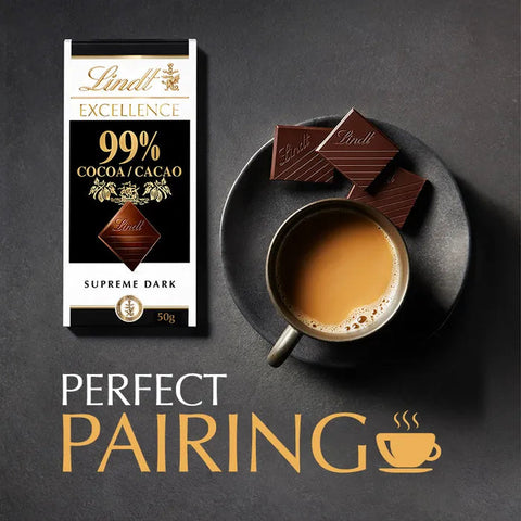 Lindt Excellence 99% Cocoa/Cacao Supreme Dark chocolate bar packaging shown next to a cup of coffee and chocolate pieces on a dark plate, with the text 'PERFECT PAIRING' on a dark gray background.