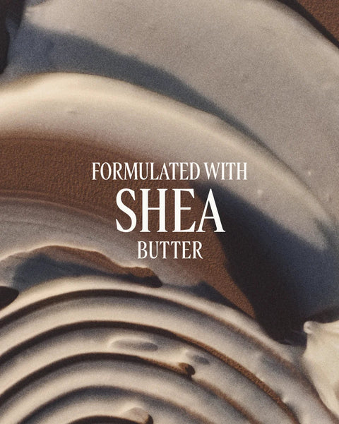 A close-up of a cream-colored cosmetic or skincare texture with text reading 'FORMULATED WITH SHEA BUTTER' in white serif lettering across the center.