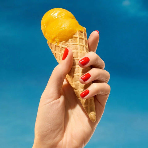 Hand holding a yellow ice cream cone against a blue sky