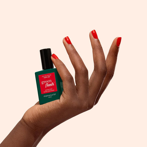 Hand holding a green and red nail polish bottle with 'green flash' text on a beige background