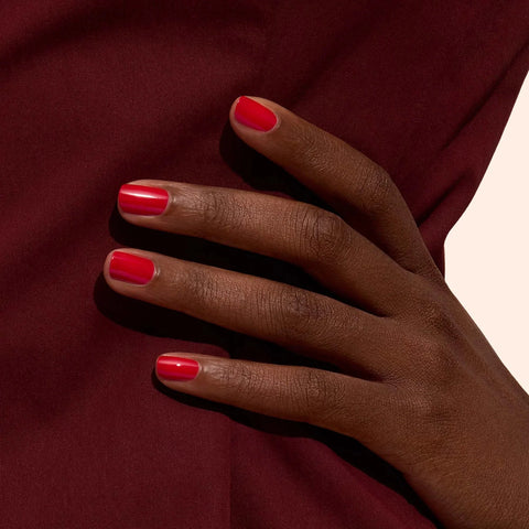 Hand with red nail polish on a maroon fabric background