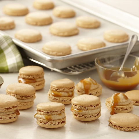 Macarons with caramel sauce on a table with a baking tray in the background