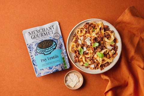 Plate of pasta with a package of Merchant Gourmet Pay Lentils on an orange background