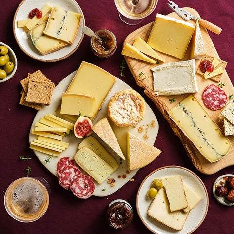 Assorted cheeses with crackers, figs, and olives on a dark surface
