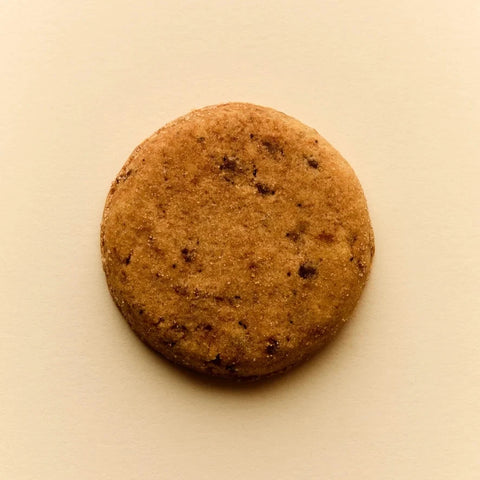 A single round brown cookie with dark chocolate chips, photographed from directly above on a plain beige background.