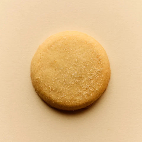 A single round golden-brown cookie with a light dusting of sugar, centered on a solid beige background.
