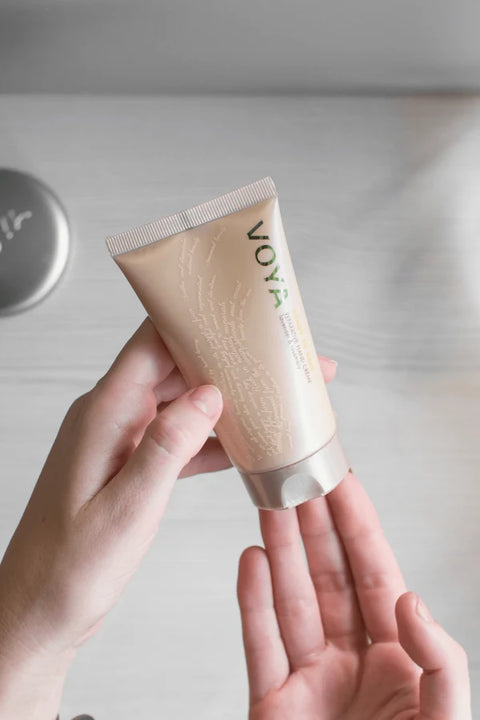 Hand holding a tube of Voya skincare product on a neutral background