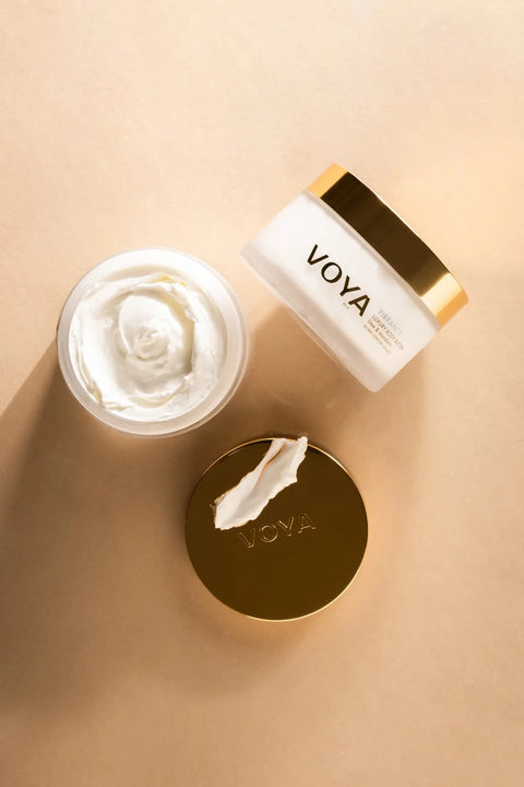 VOYA skincare cream jar set on a warm beige background, featuring a white jar of cream, its gold lid, and the white jar with a gold lid, all branded with VOYA.