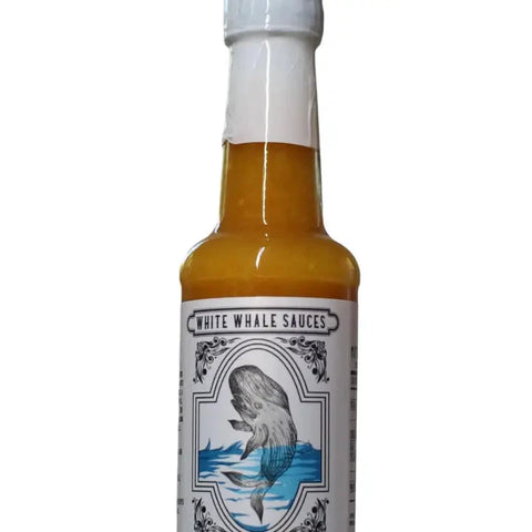 A bottle of White Whale Sauces hot sauce with amber-colored liquid inside, a white cap, and a white label featuring a whale illustration.